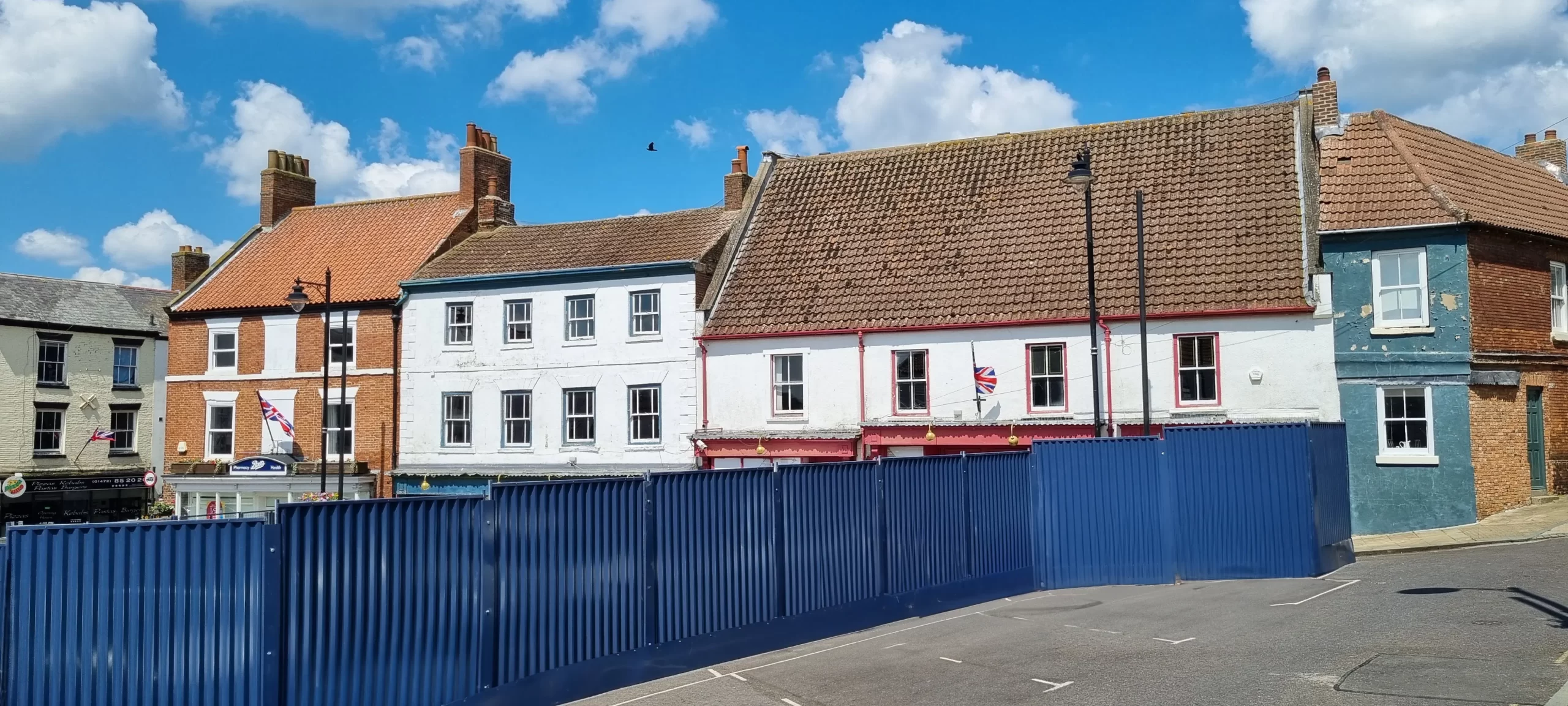 Front of the buildings with blue metal hoardings forming a compound.